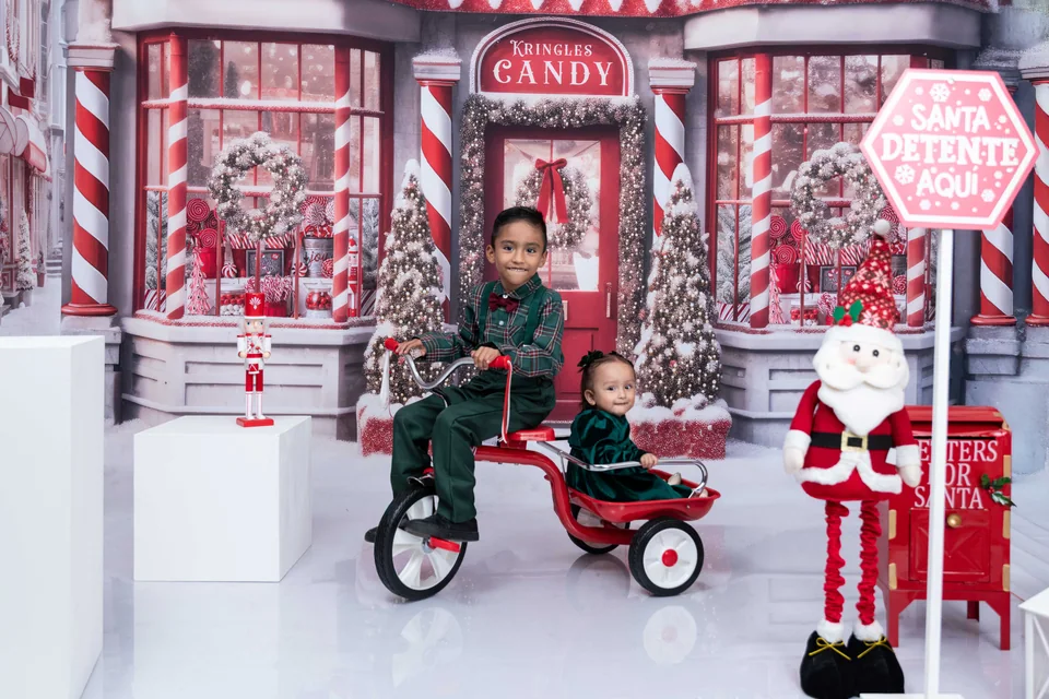 Dos niños con un triciclo en un escenario de dulces navideños.