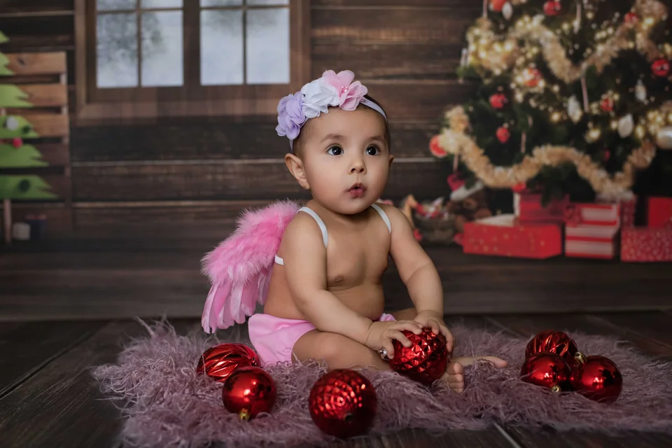 Un bebé con accesorios rosas y esferas rojas de Navidad.